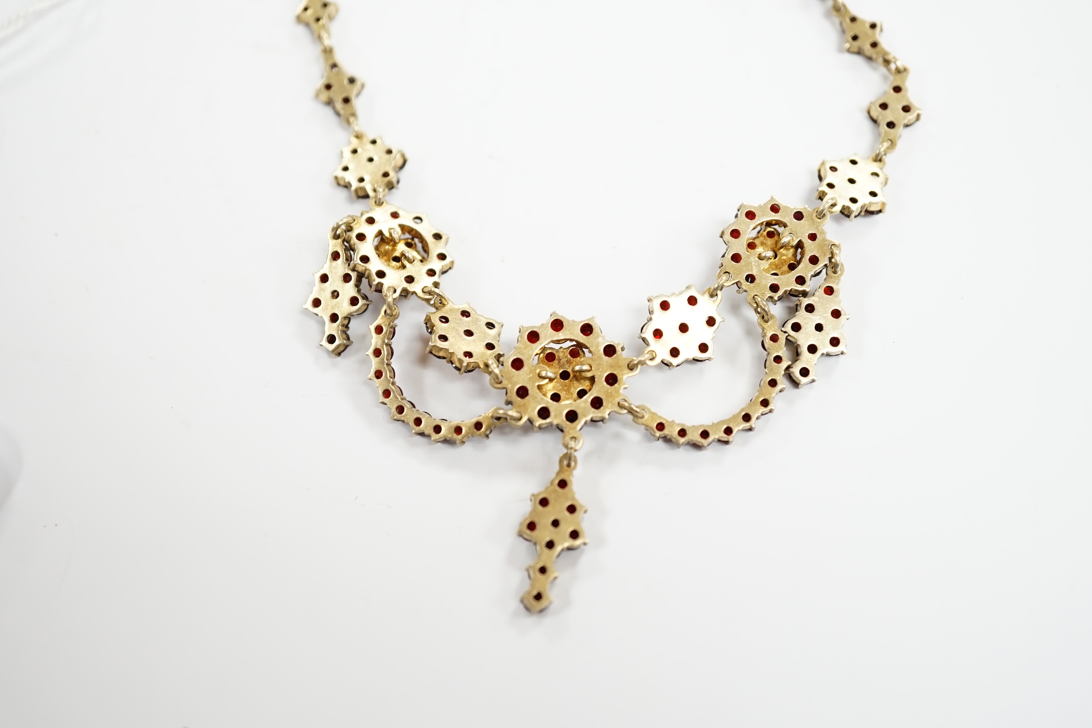 An early 20th century gilt sterling and garnet cluster set drop necklace, 45cm.